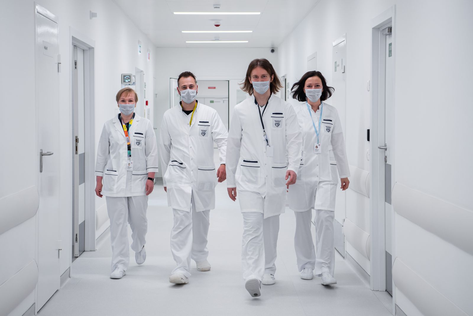 Four clinical staff in white coats walking a hospital corridor together at the start of a shift.