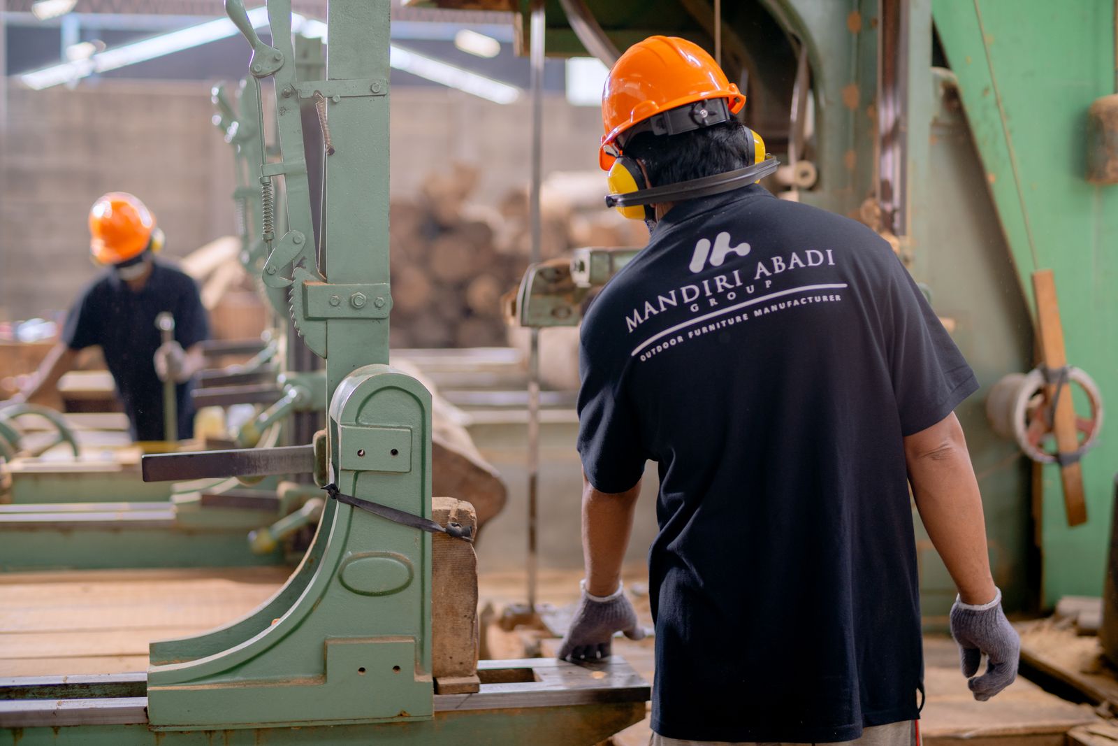 An experienced worker in a hard hat showing another how to set up a machine on a workshop floor.